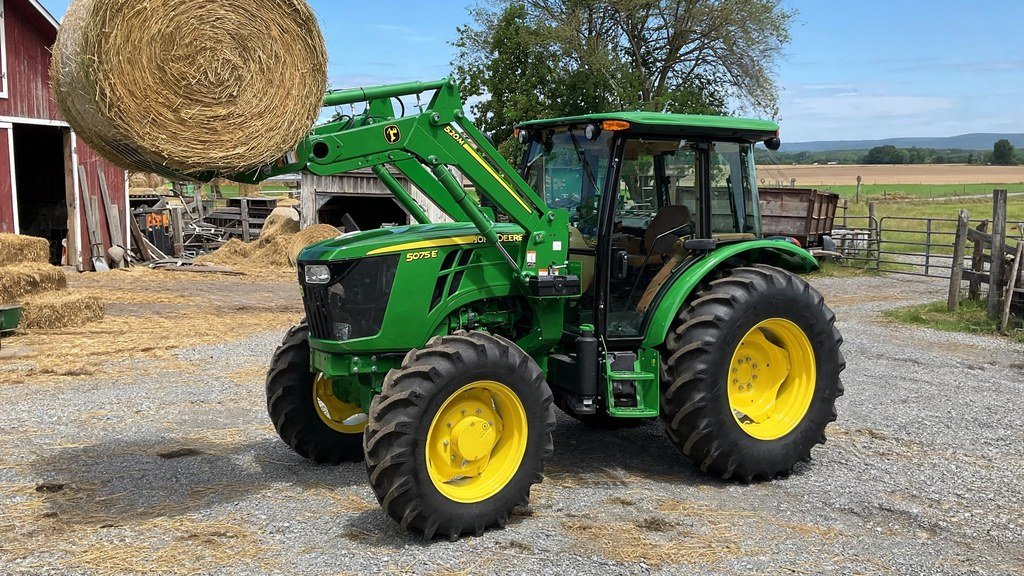 John Deere 5075E with 520M front loader carrying a round hay bale